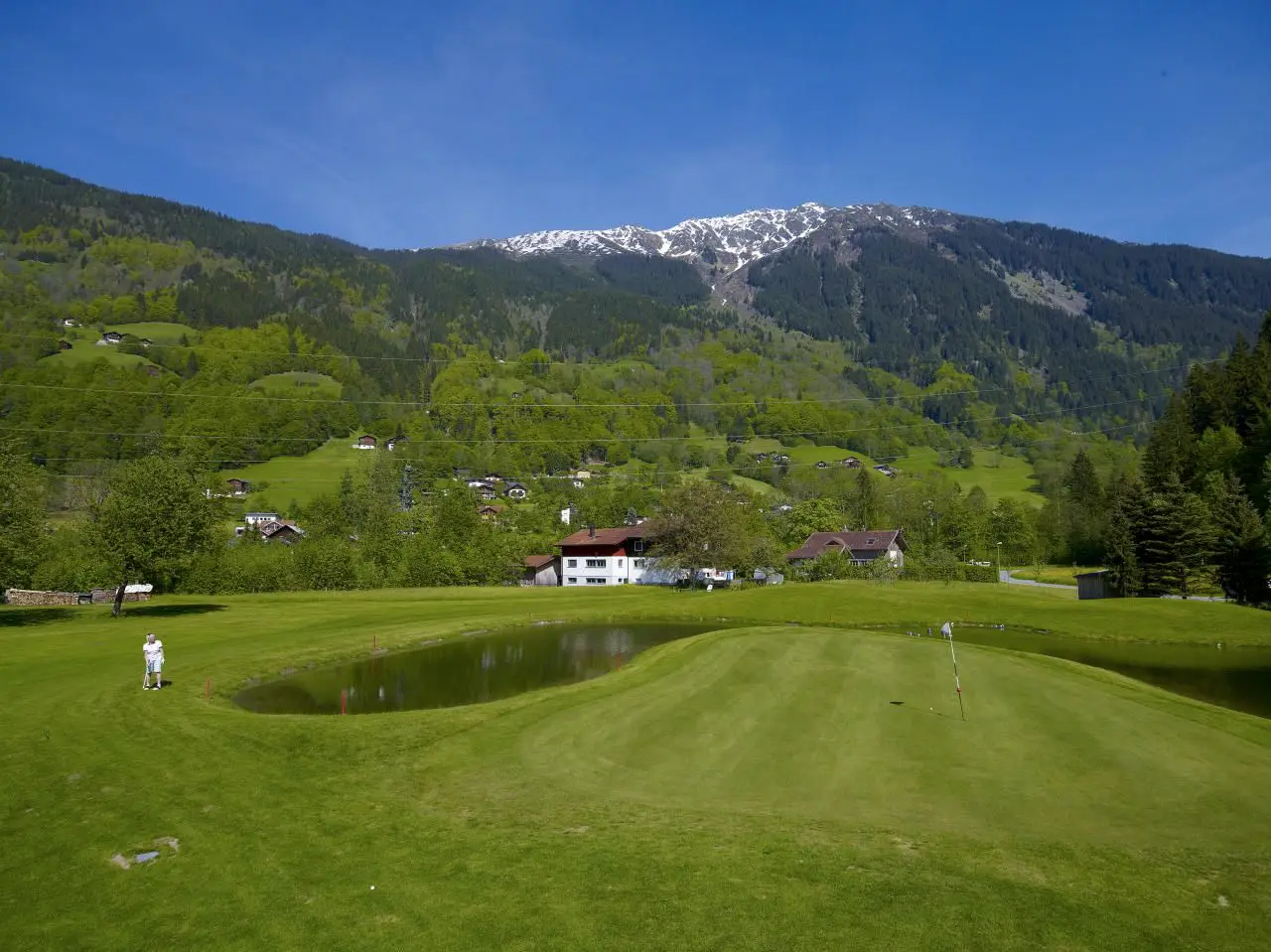 Grün am Teich, dahinter Häuser von Tschagguns und die Berge