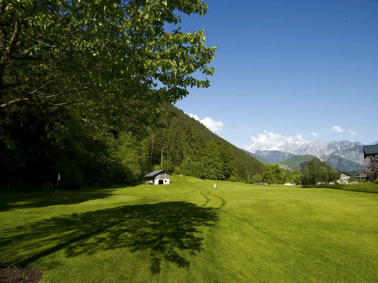 Langes Fairway mit dem Schatten eines Baumes, dahinter die Berge