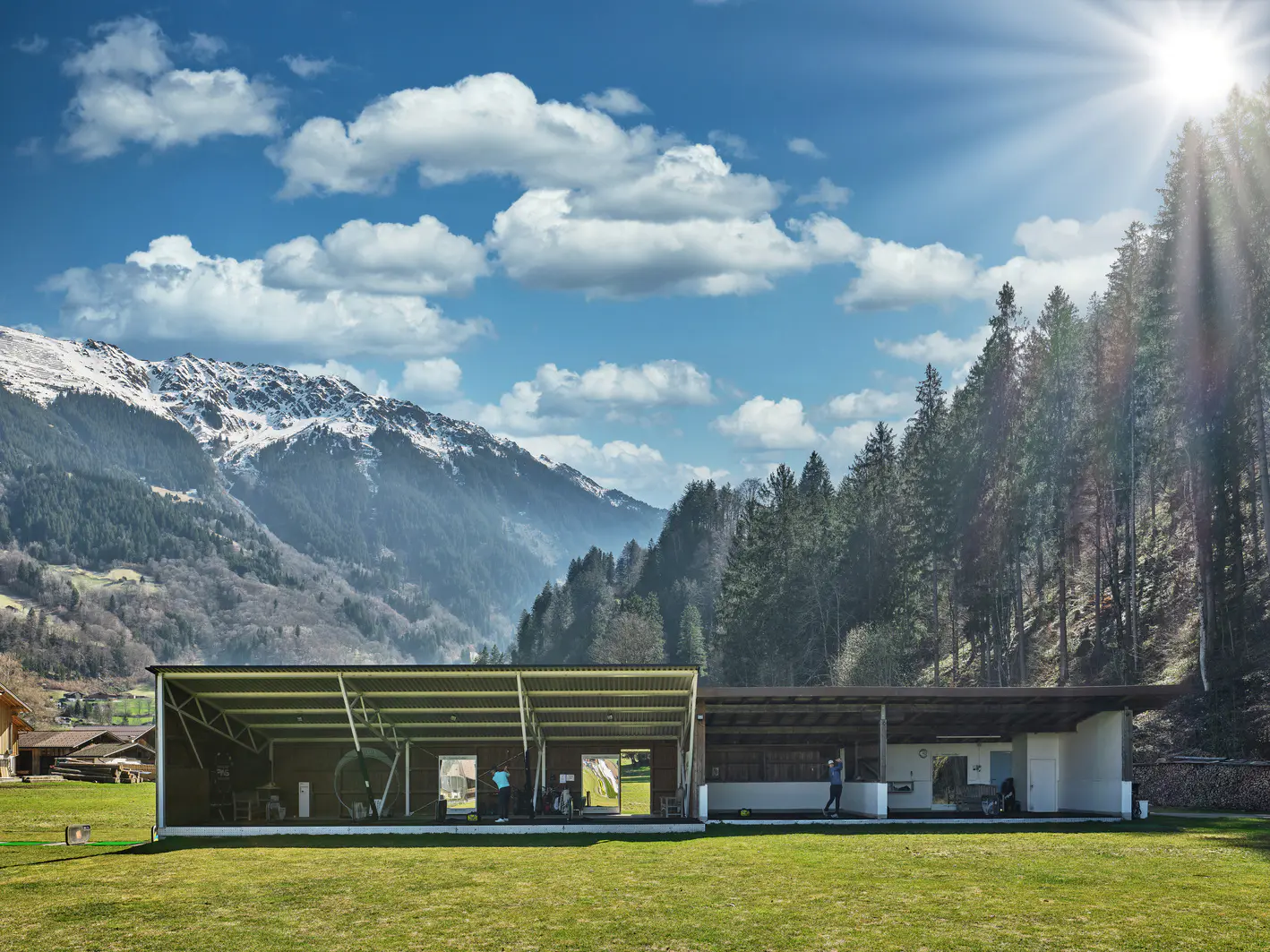 Driving Range mit überdachten Abschlägen vor Wald und Bergen