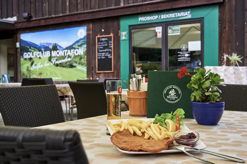 Schnitzel mit Pommes auf der Terrasse, dahinter Proshop und Sekretariat